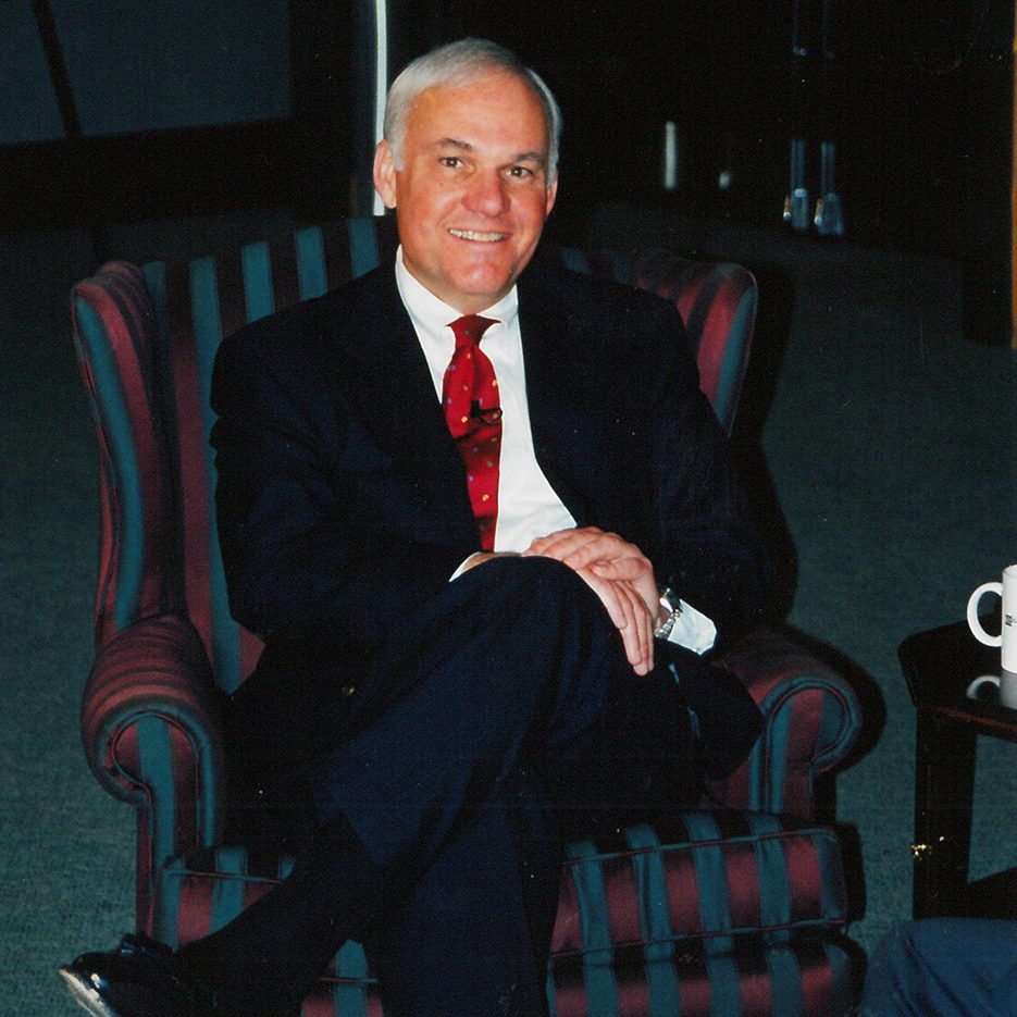 Andy Taylor sitting in a chair with a dark suit and red tie