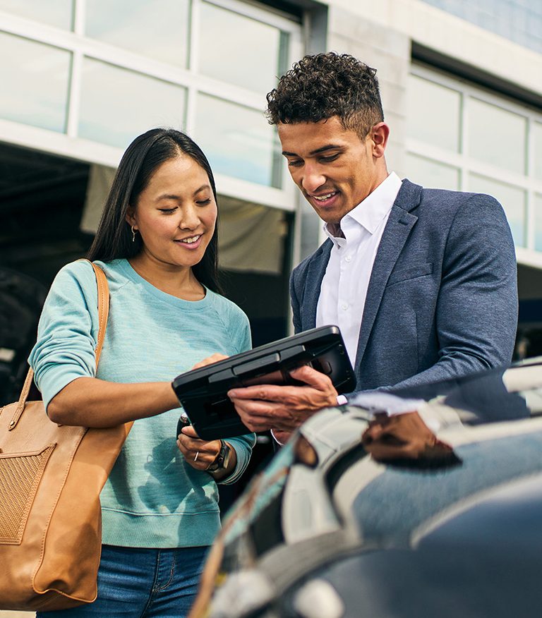 A woman and man look over an iPad at a car lot