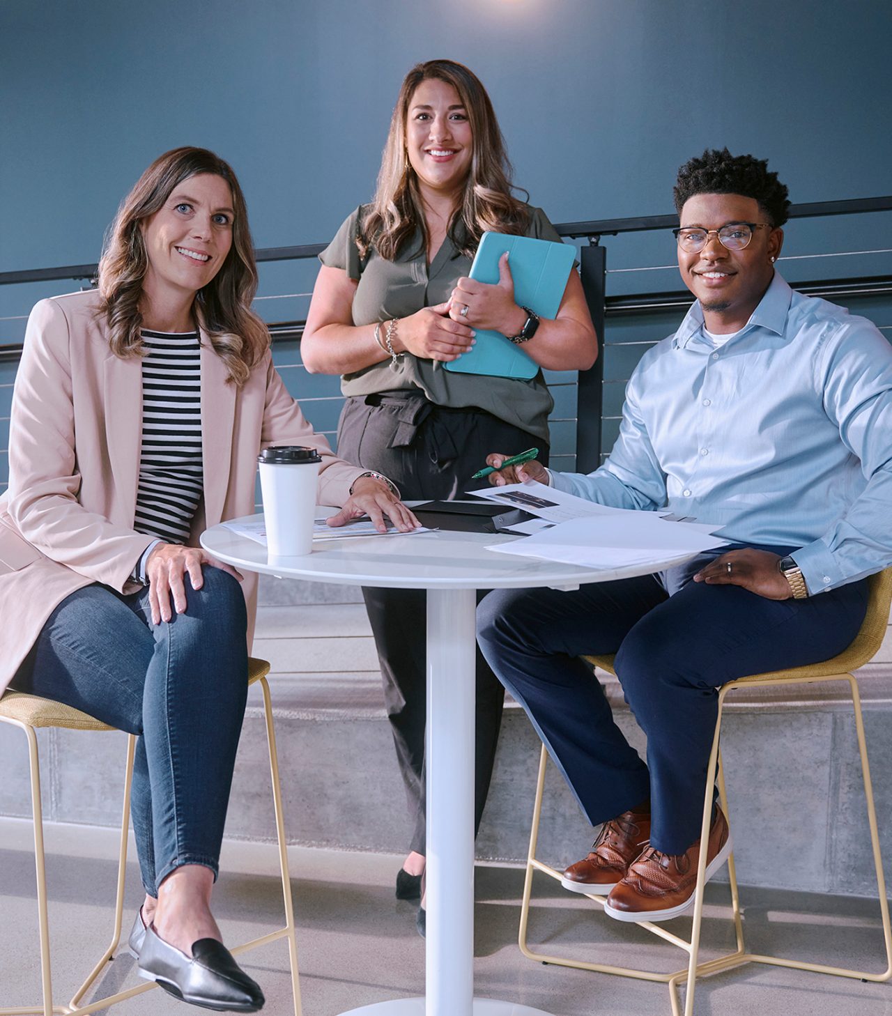 Two female employees and one male employee smiling and gathered around a tall white table.