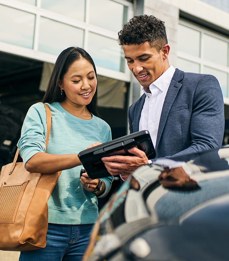 A male employee holds an iPad in front of him while having a conversation with a female customer