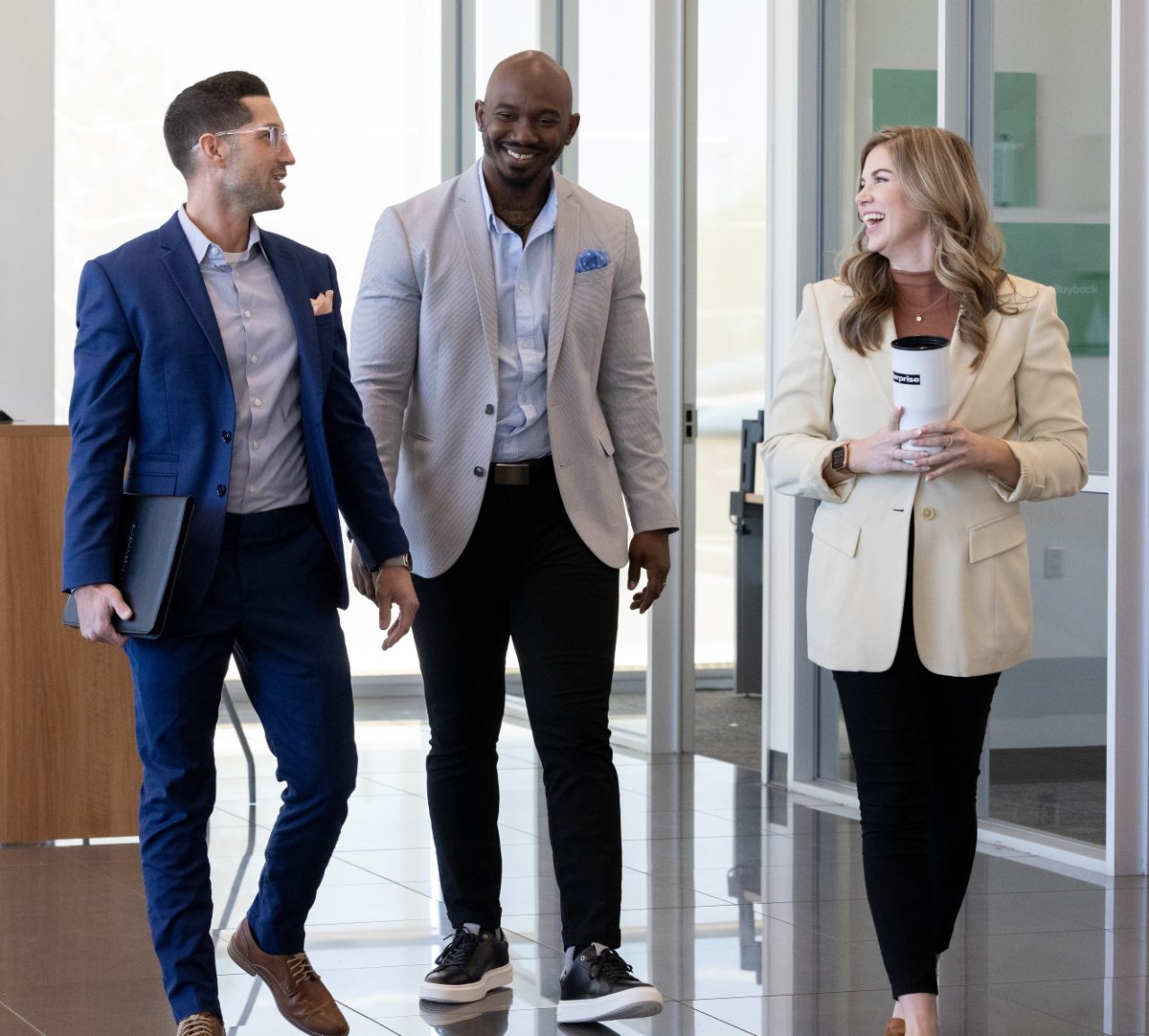 Two male and one female team member talk and laugh while walking through a lobby