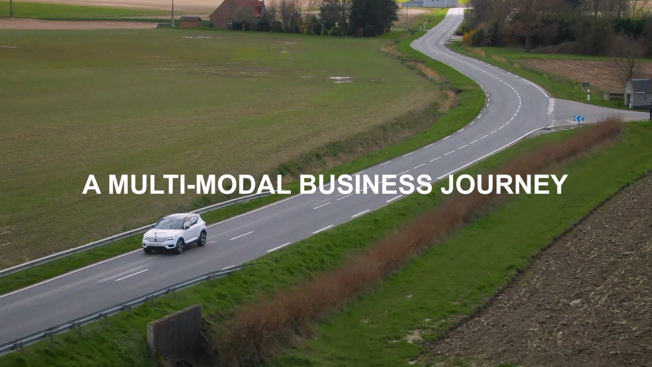 A white car drives on the road with green grass all around