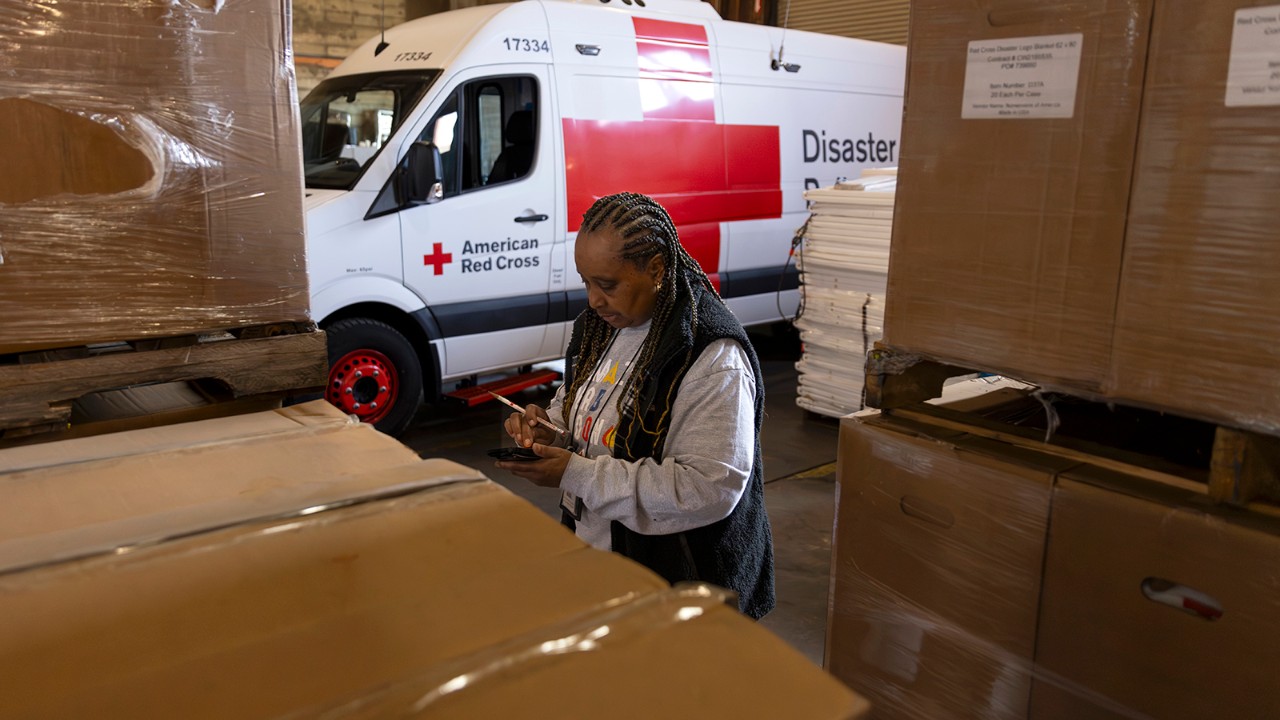 A lady, texting from her cell phone, stands in front of a white American Red Cross van