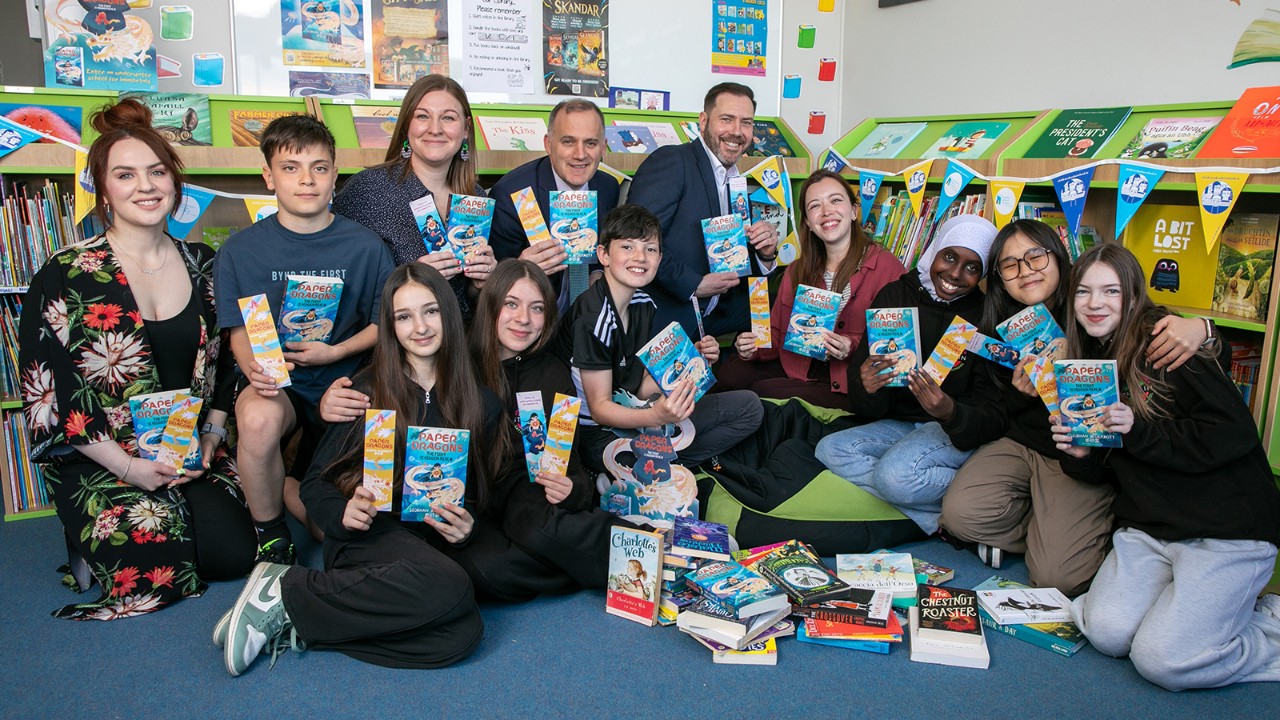 Sevel adults and children smile while holding up their books