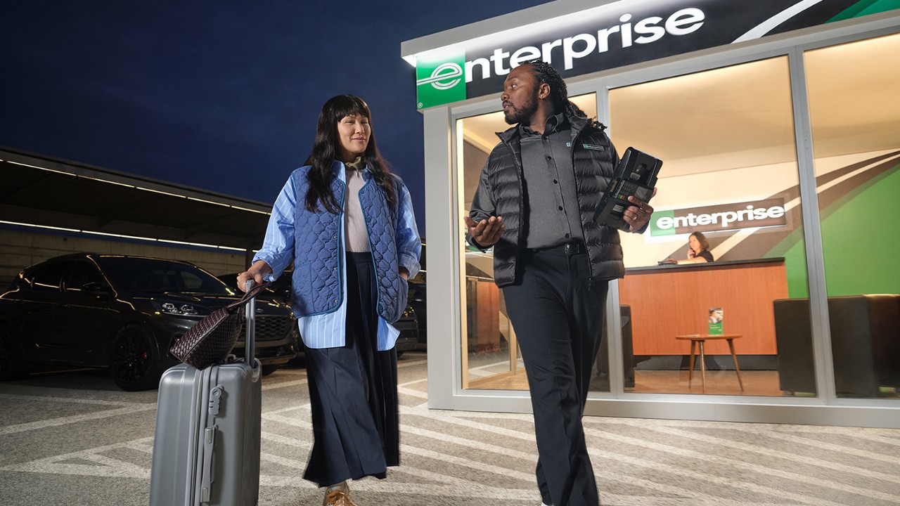 A female customer and male employee talk in an Enterprise Rent-A-Car parking lot after dark