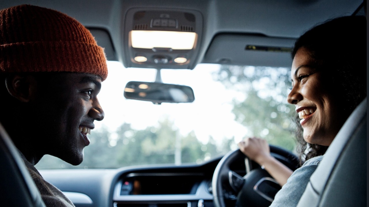 A man and woman in the United Kingdom talk inside a car