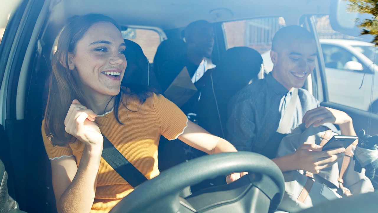 A woman driver in the United Kingdom laughs with a man in the passenger's seat on a sunny day