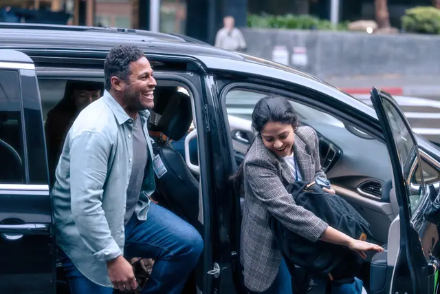 Dos hombres sonrientes, uno saliendo del asiento de pasajero de una van y el otro saliendo del asiento de en medio.